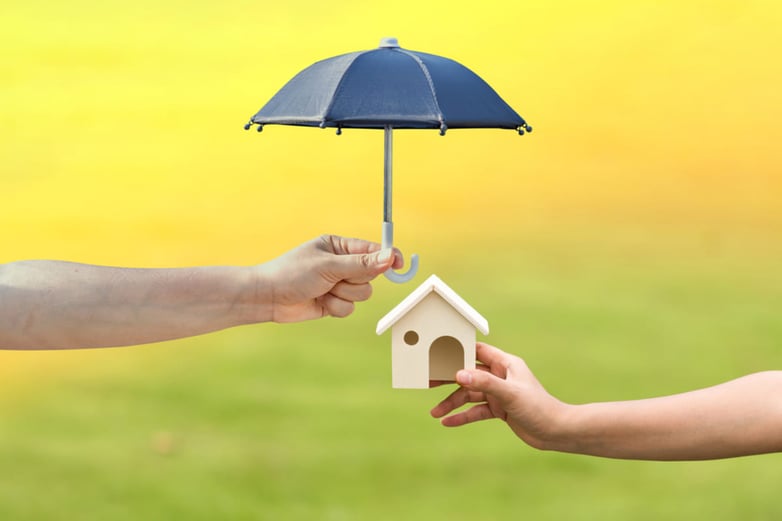 Someone holding a paper umbrella over a model house, property management company concept