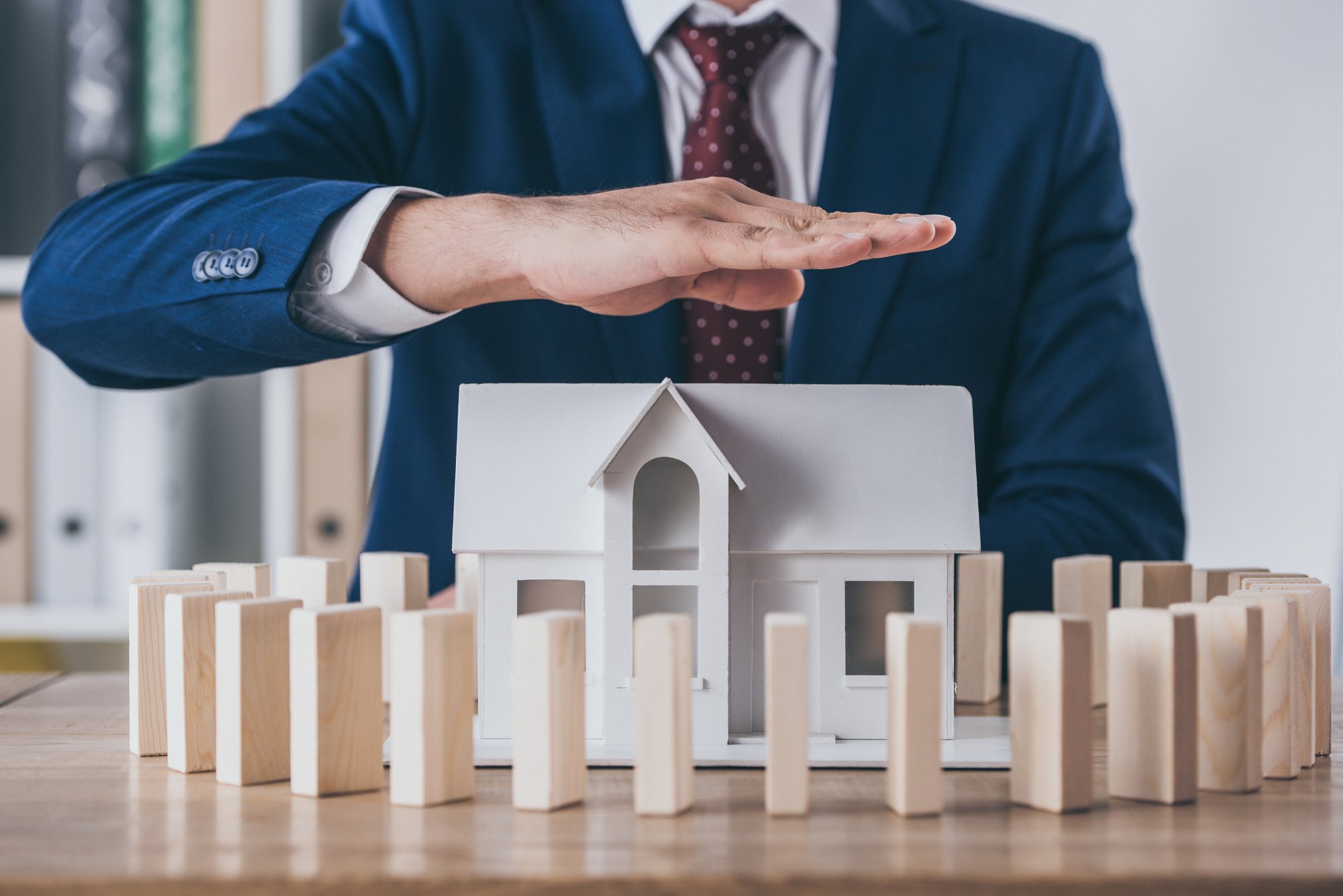 Cropped view of risk manager covering house model surrounded with wooden blocks with hand