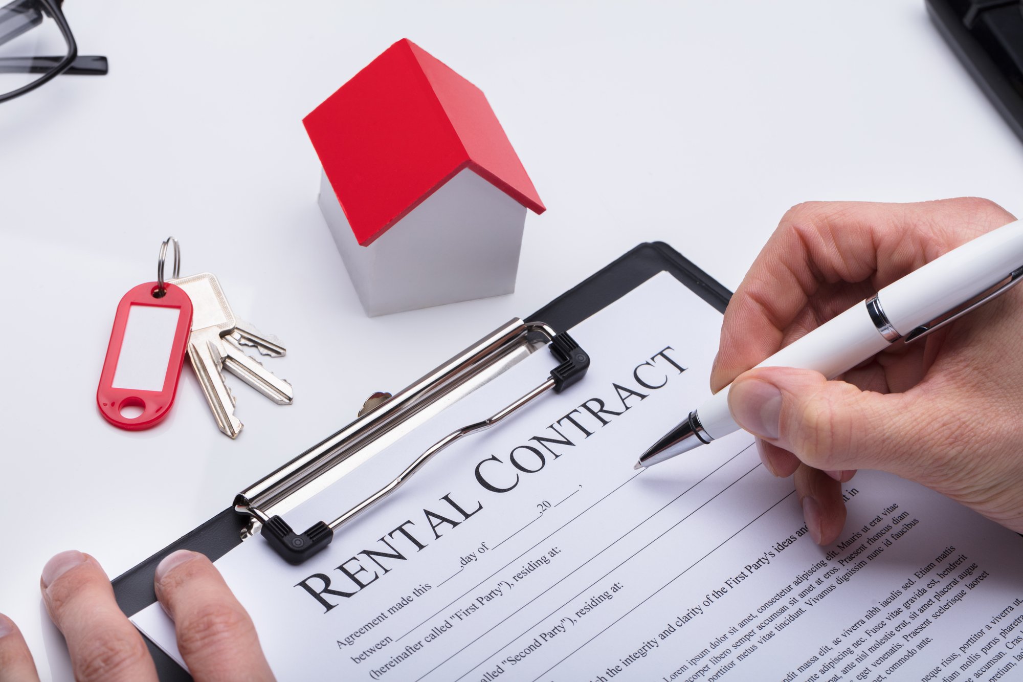 Human Hand Filling Rental Contract Form With House Model And Key On Desk