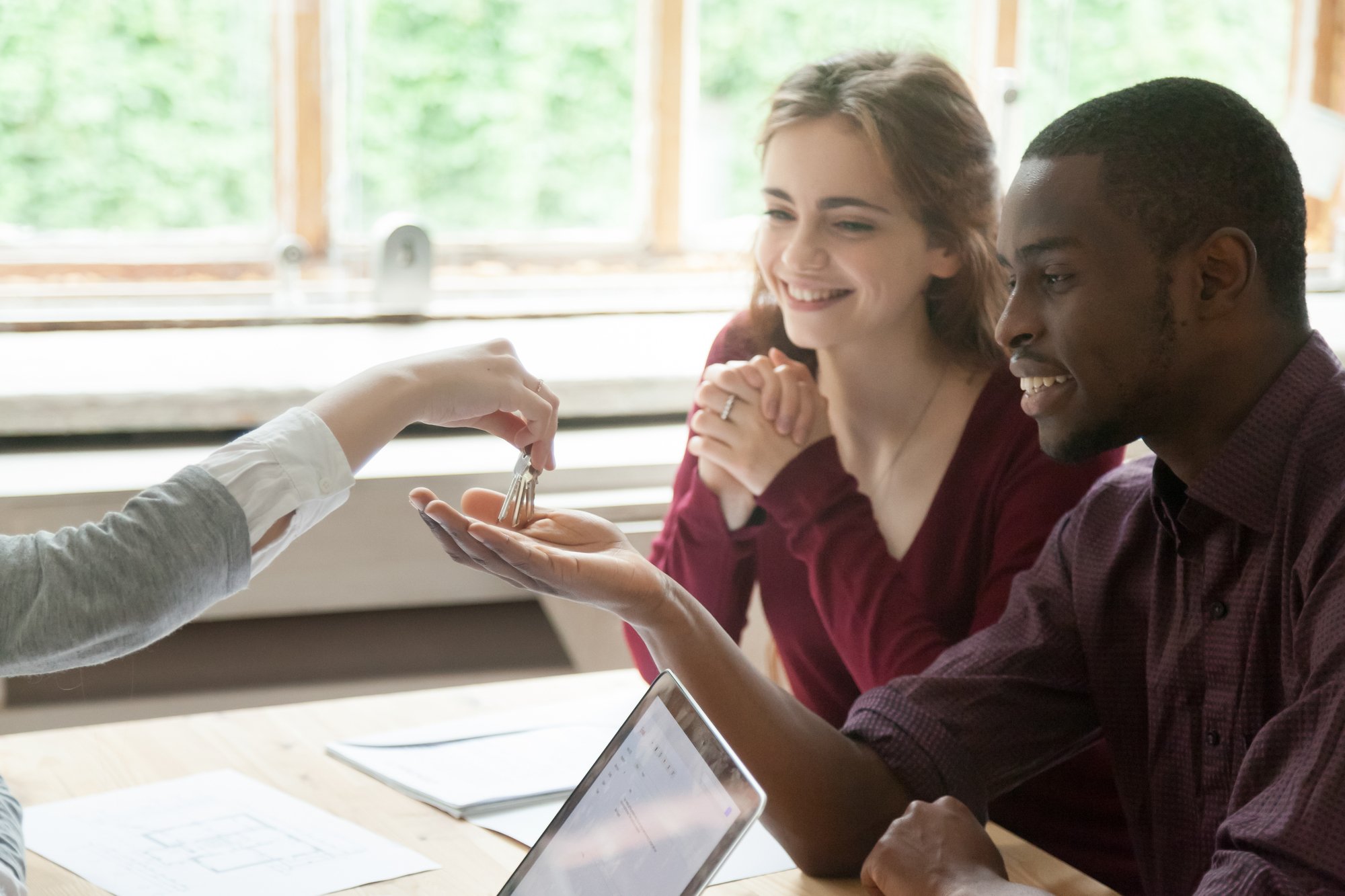 Real estate agent handing house keys to happy multiethnic couple