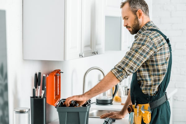 Side view of handsome plumber taking tools from toolbox in kitchen