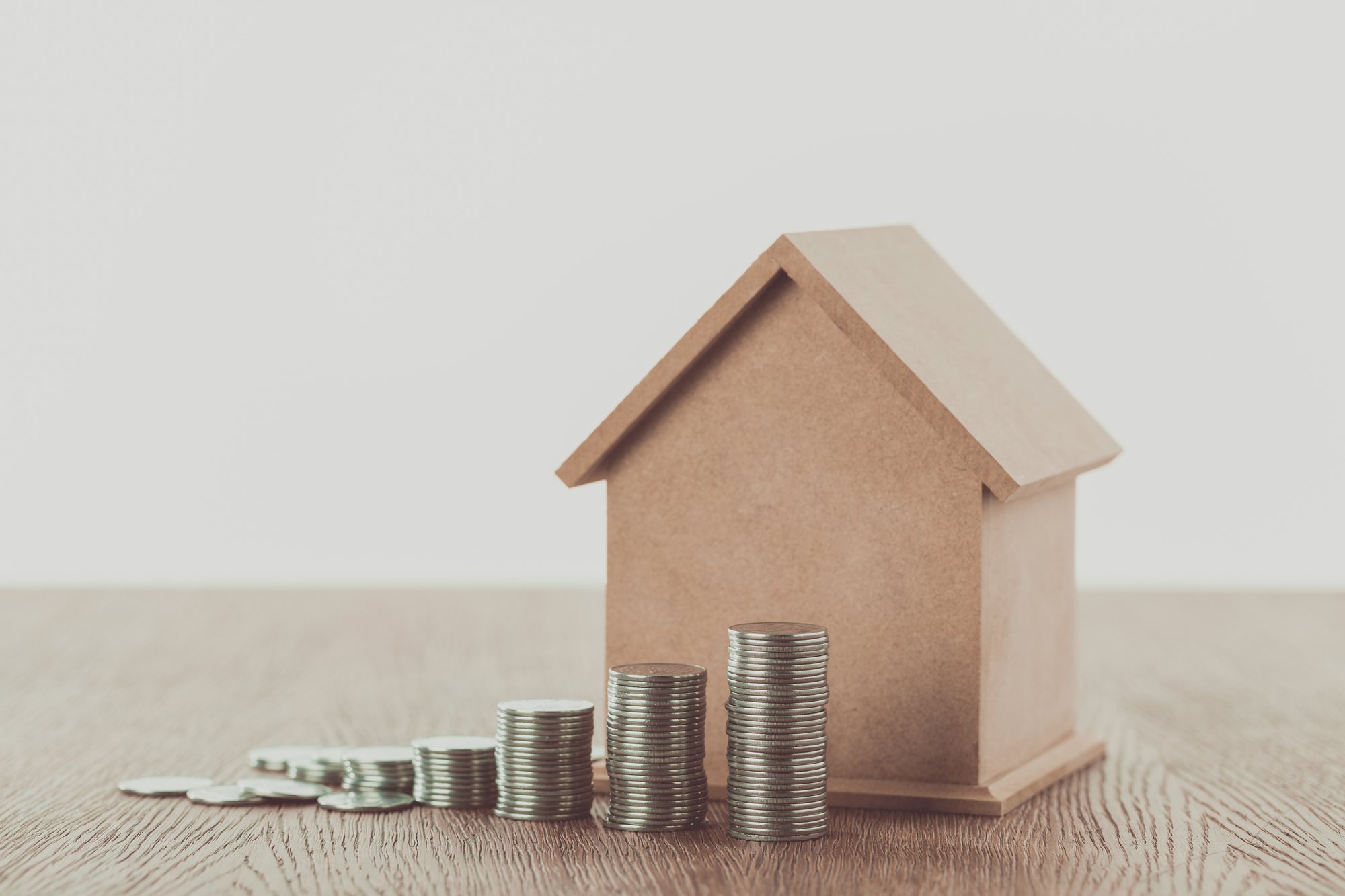 Stacks of coins and small house on wooden table, saving concept