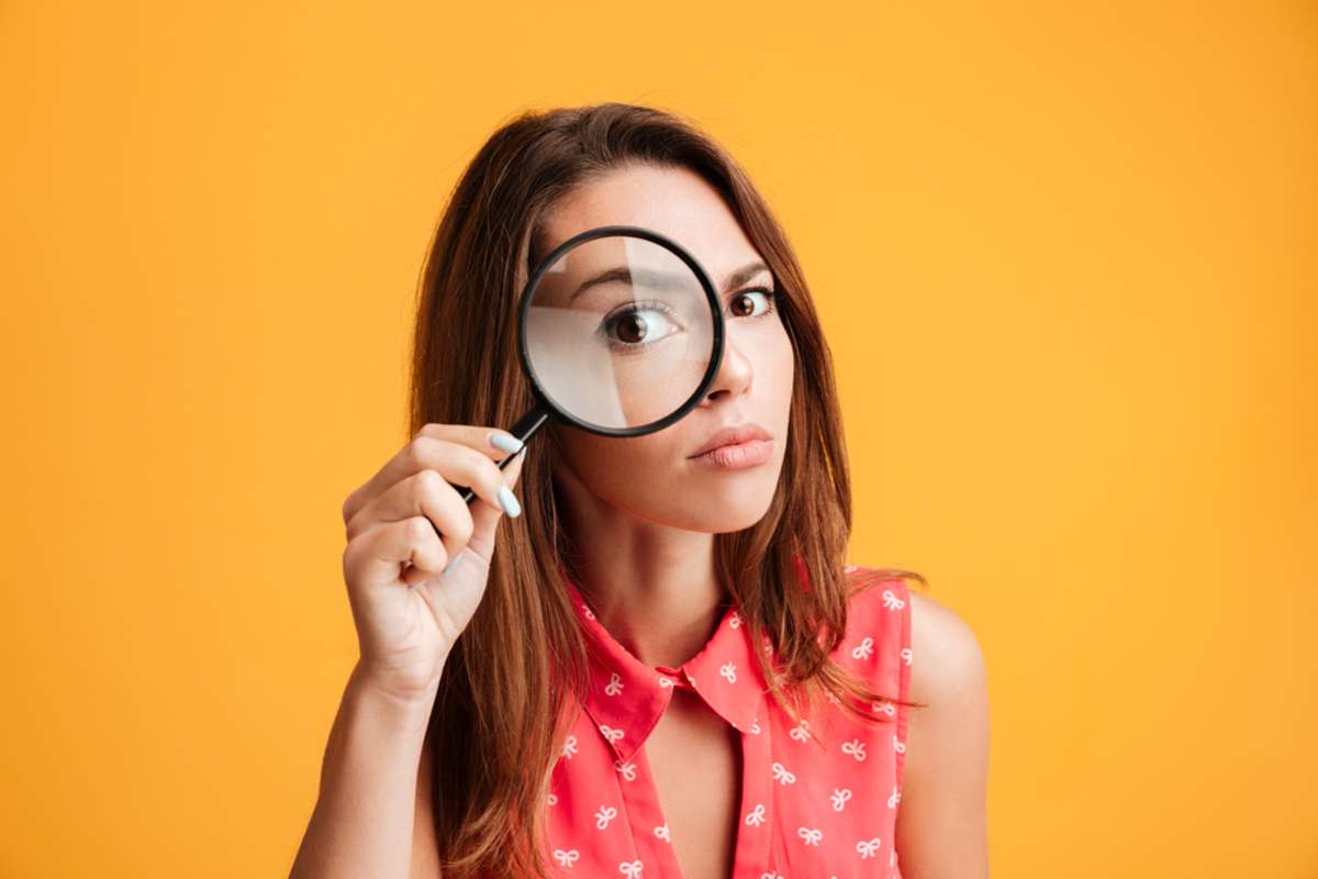 Close-up portrait of young serious woman looking through a magnifying glass