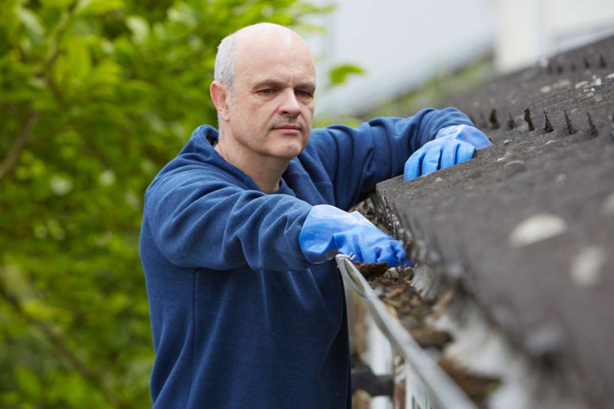 Man cleaning house gutters, rental property maintenance concept