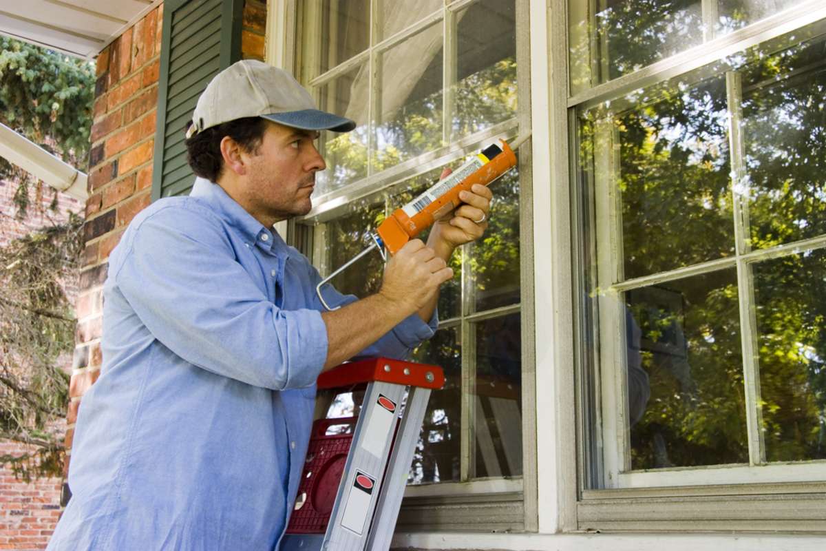 Man on ladder caulking outside window