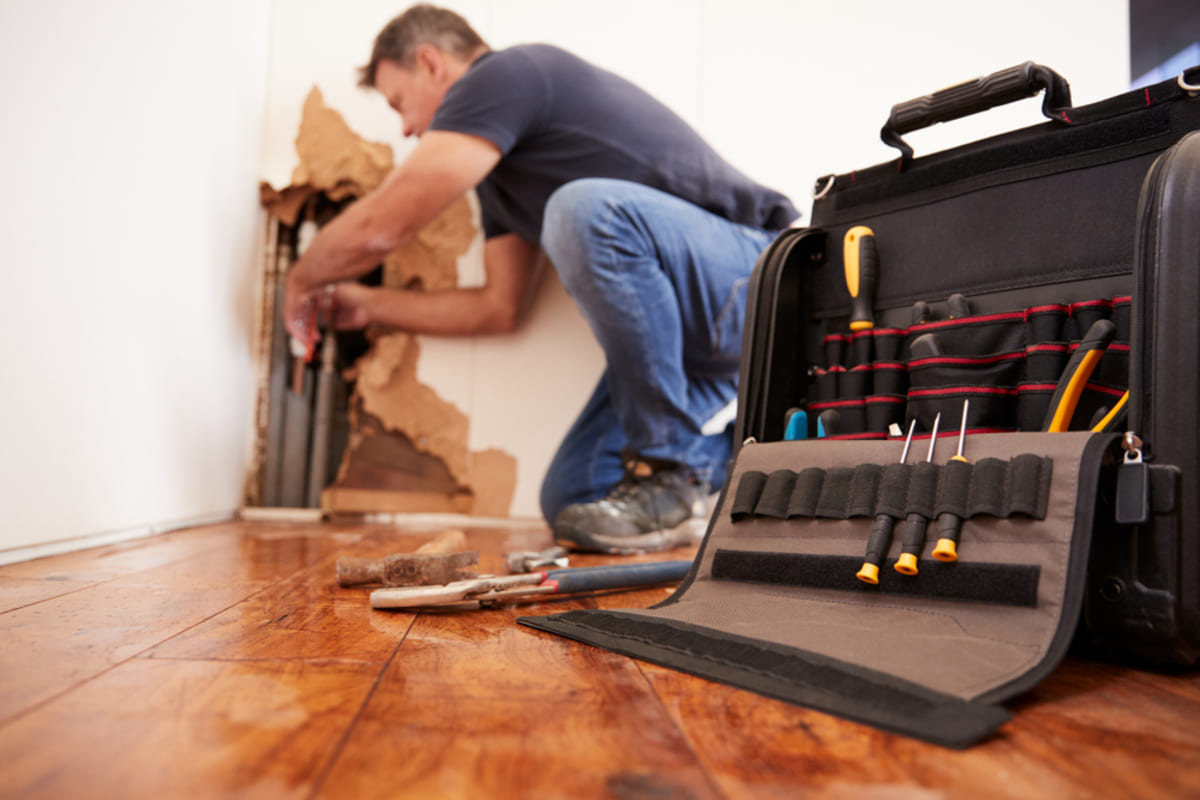 A man repairing a burst pipe with a tool kit in front - featured_image