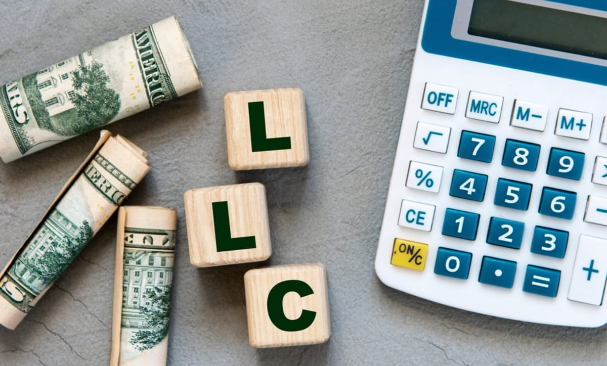 LLC (Limited Liability Company) on wooden cubes on gray background with calculator and banknotes