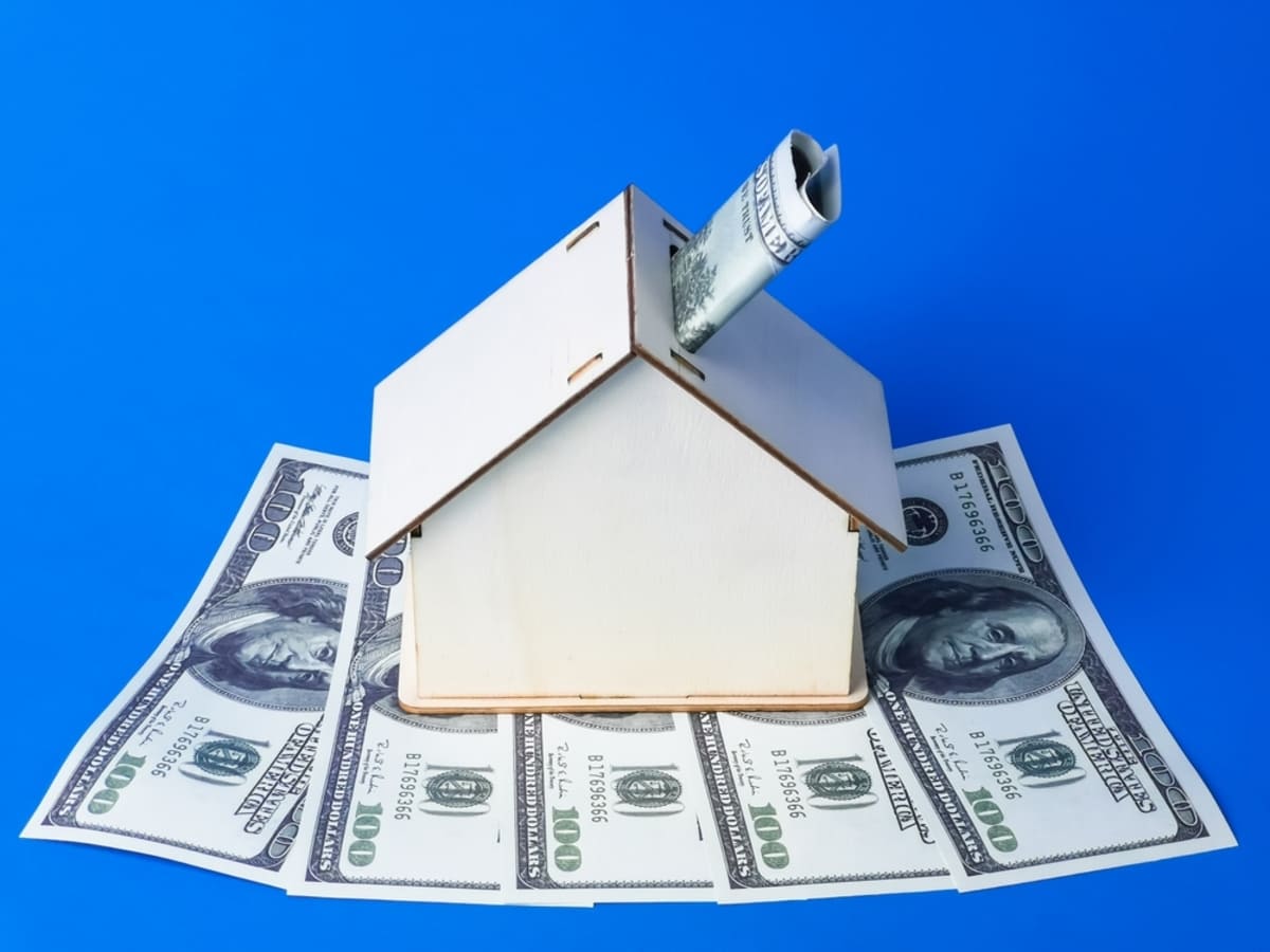 Miniature house with dollars. Budgeting for residential roof maintenance
