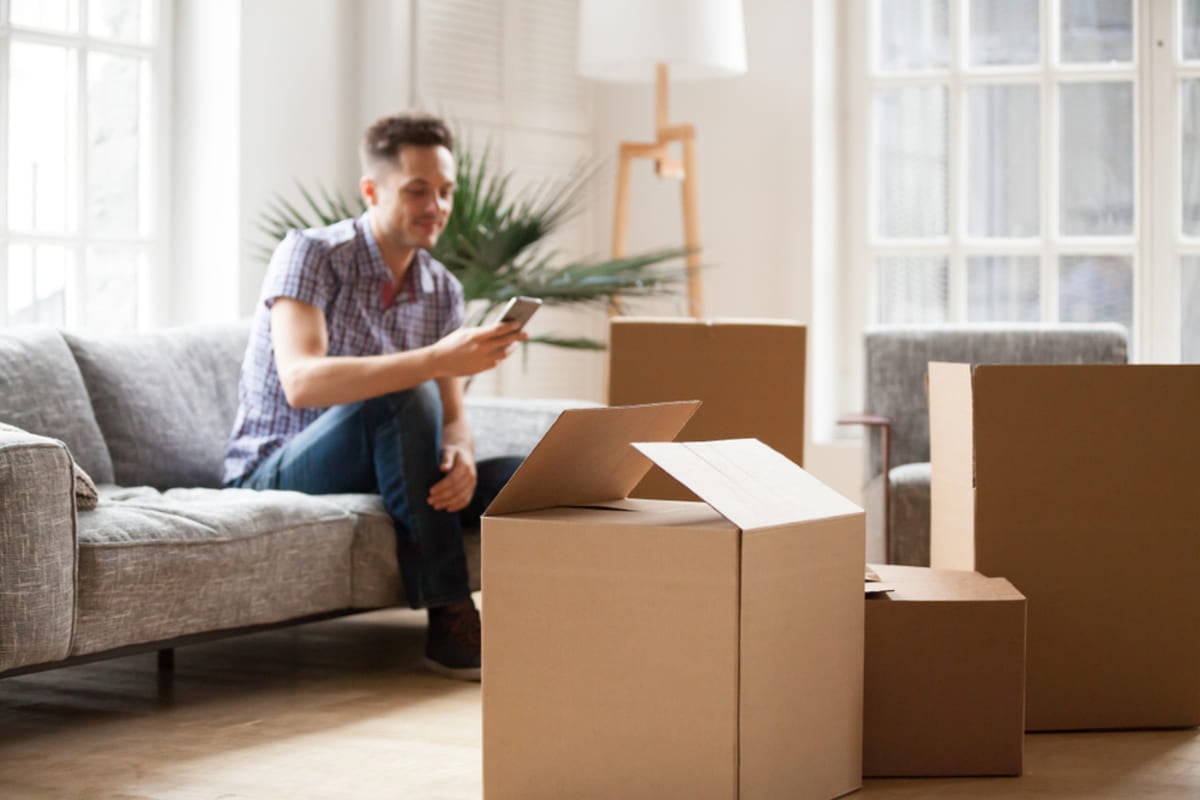 Packed cardboard boxes with young man sitting on sofa