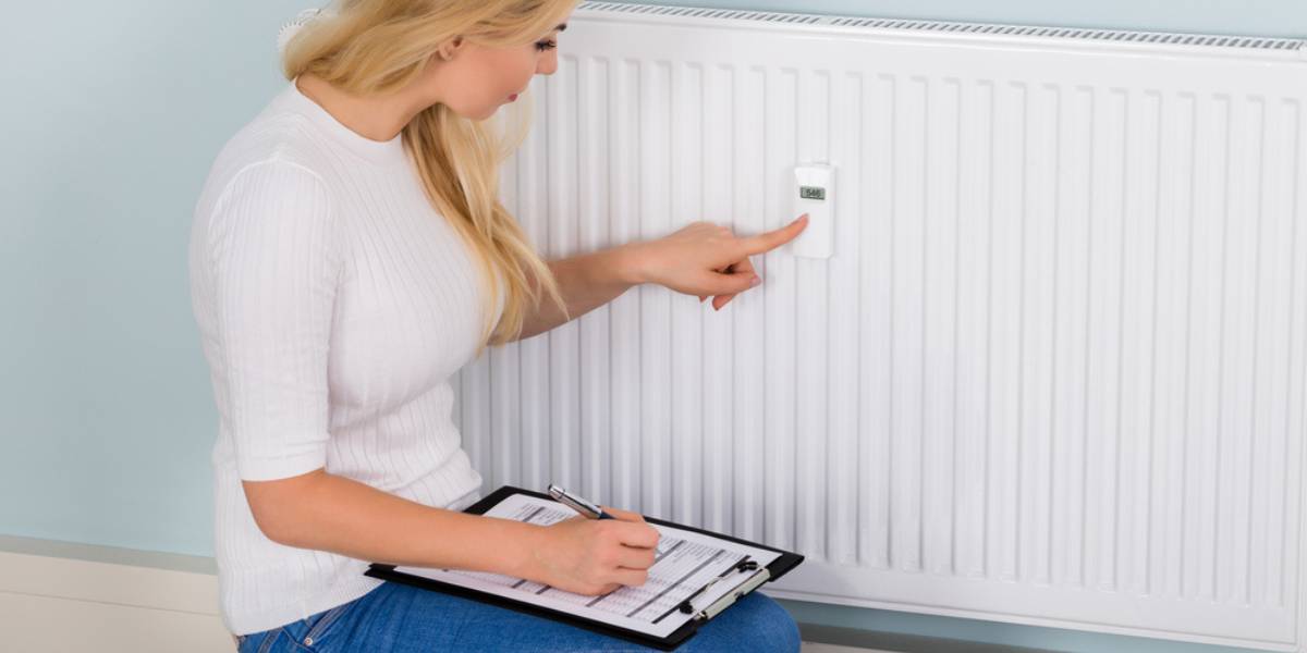Young Woman Maintaining Records Of Digital Thermostat On Clipboard At Home