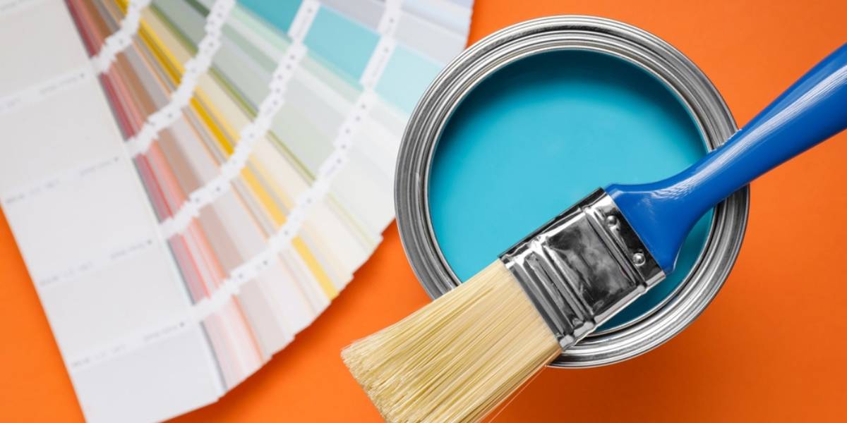 Can with light blue paint, brush and color palette on orange background