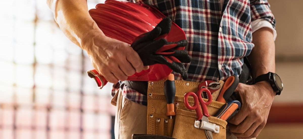 Closeup of bricklayer hands holding hardhat and construction equipment