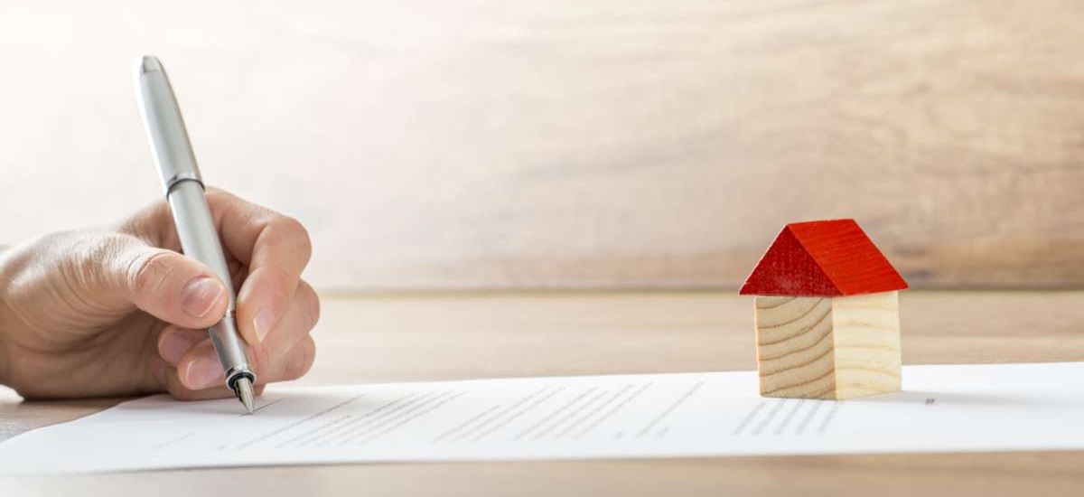 Closeup of new homeowner signing a contract of house sale or mortgage papers with a wooden toy house on the document