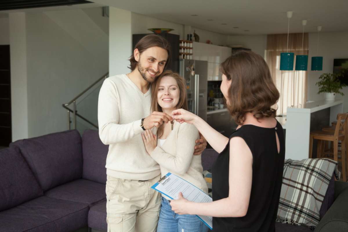 Happy young couple becoming tenants getting own keys of new home at meeting with real estate agent indoors